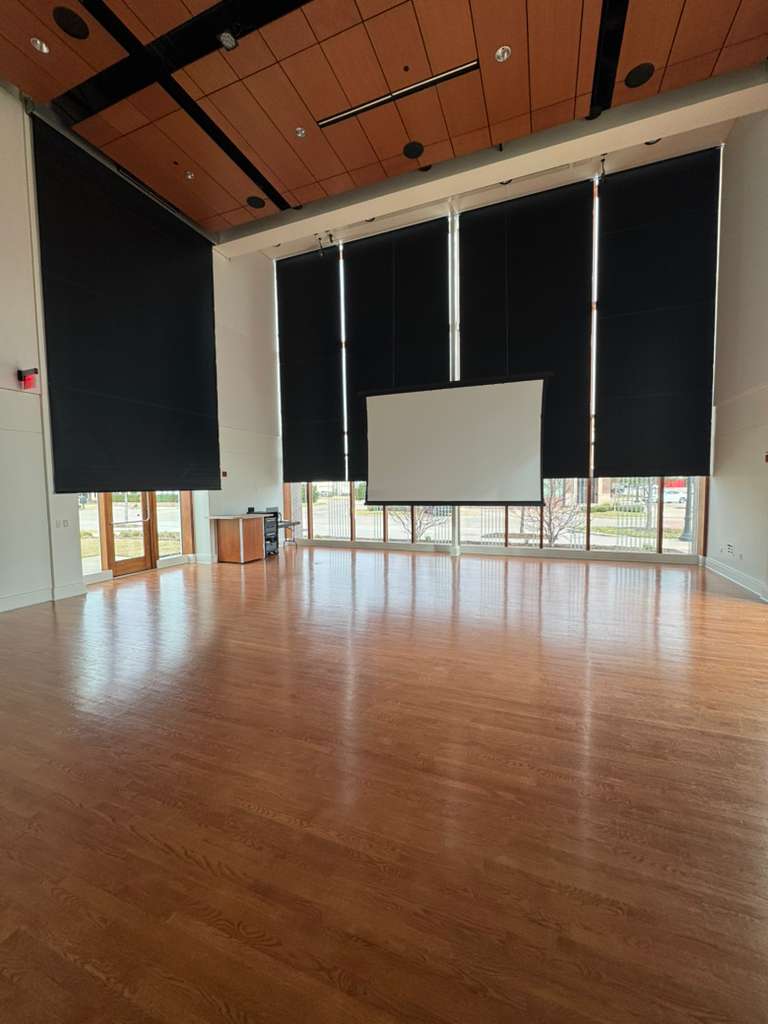 Blackout roller shades on tall windows in a city event hall with a projector screen