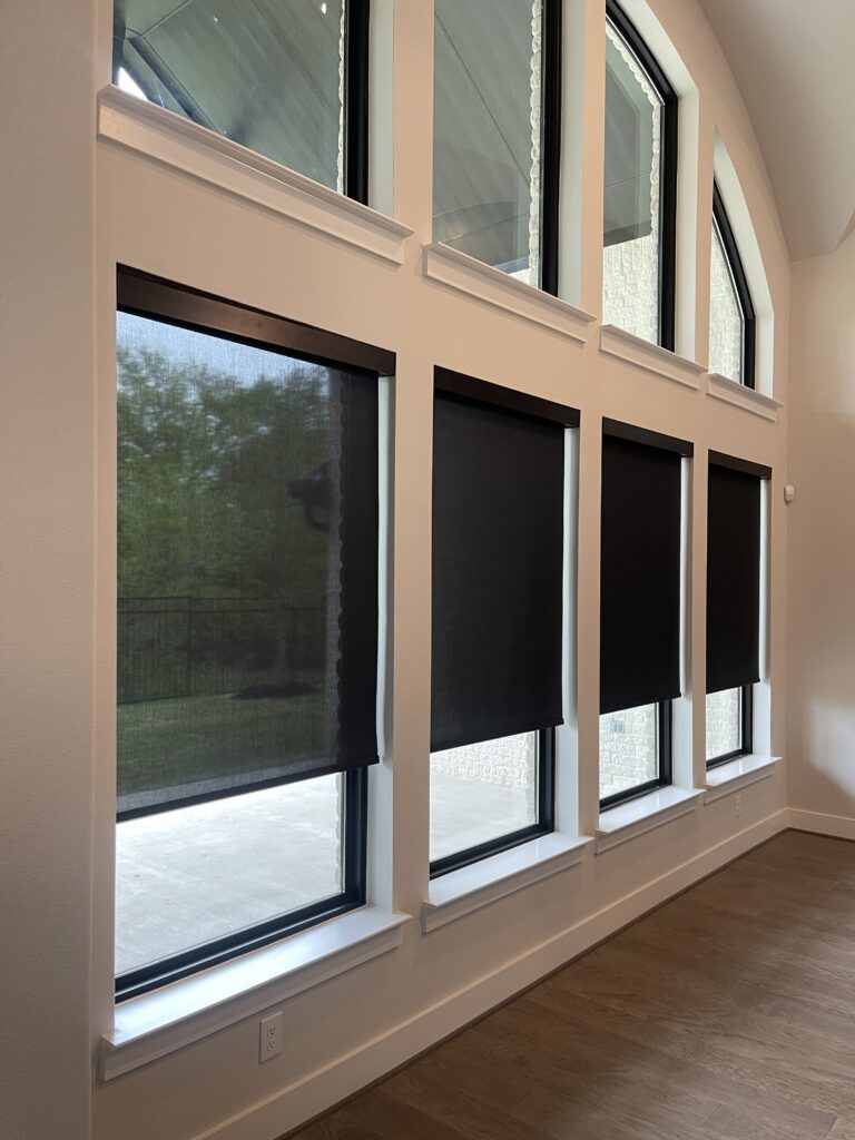 Dark roller shades on tall windows in a two-story room with open transom windows above