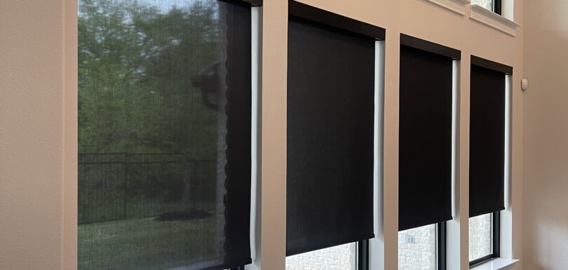 Dark roller shades on tall windows in a two-story room with open transom windows above