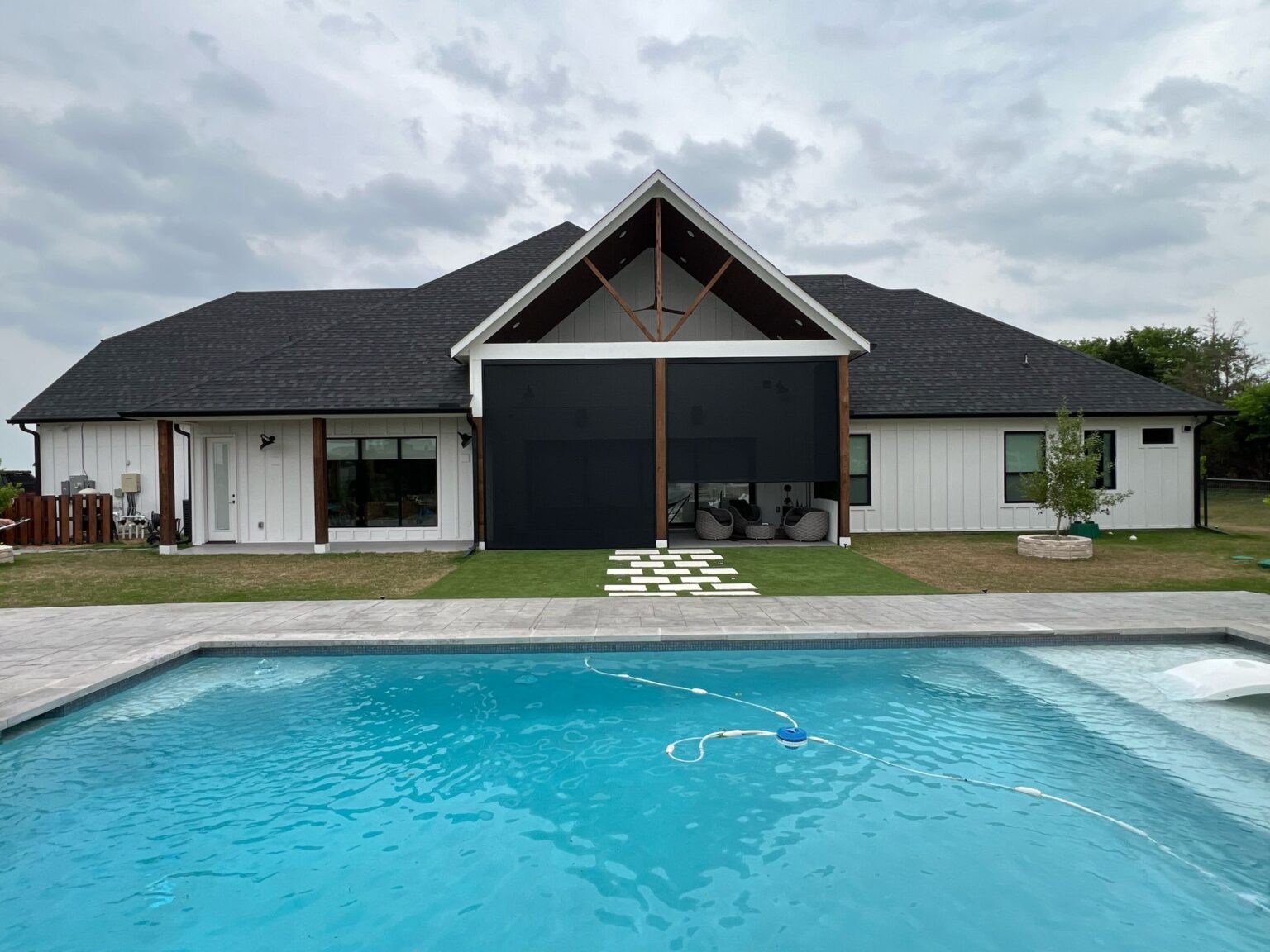 Two black zip-track screens on a farmhouse covered patio facing a pool, installed by Shadeotech