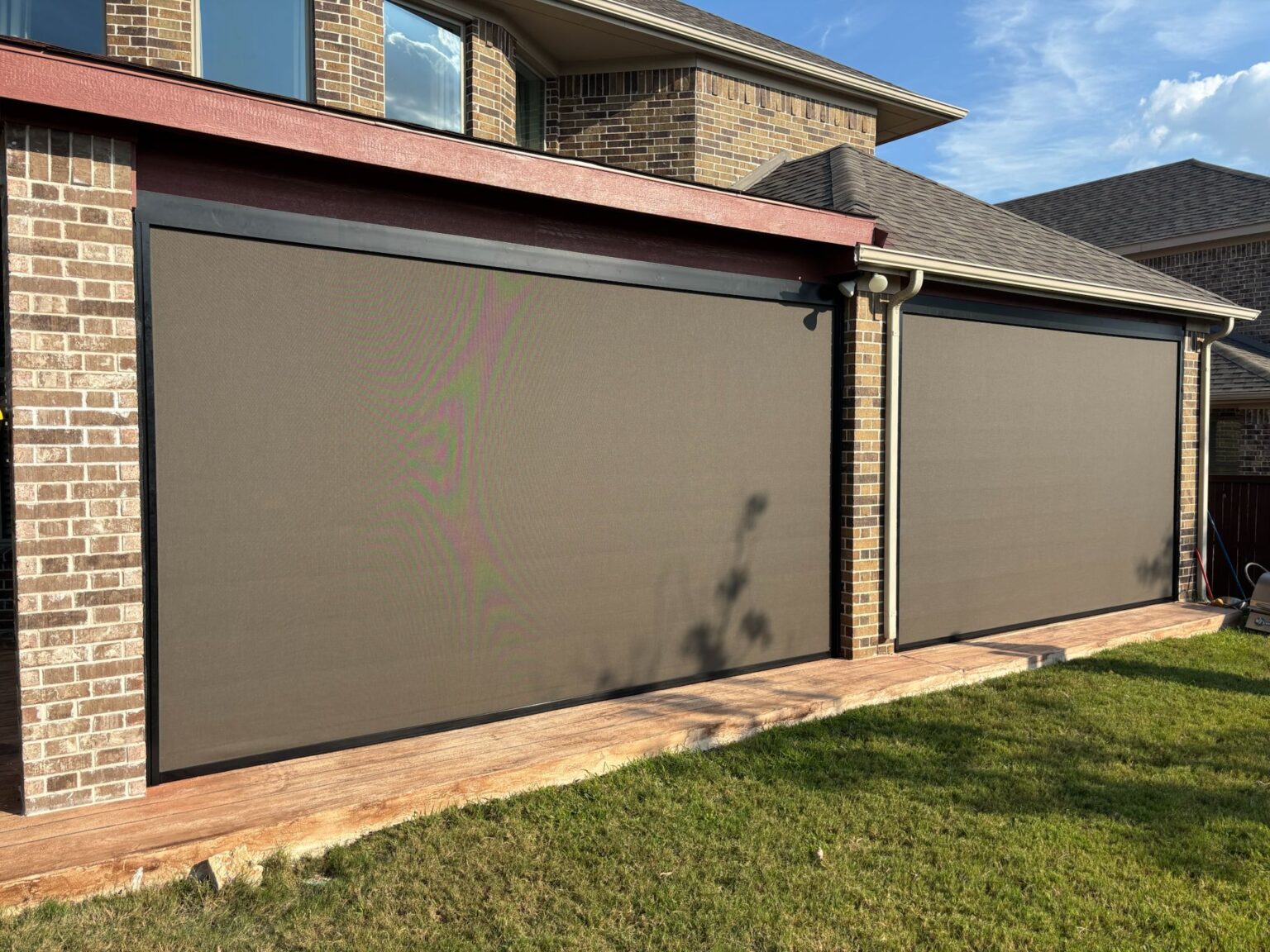 Two bronze motorized zip-track screens fully lowered on a two-bay patio, by Shadeotech